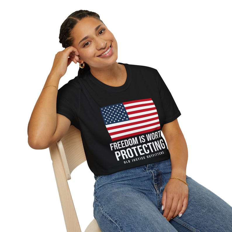 Woman wearing a black Old Justice Outfitters T-shirt with an American flag and FREEDOM IS WORTH PROTECTING lettering on the front.